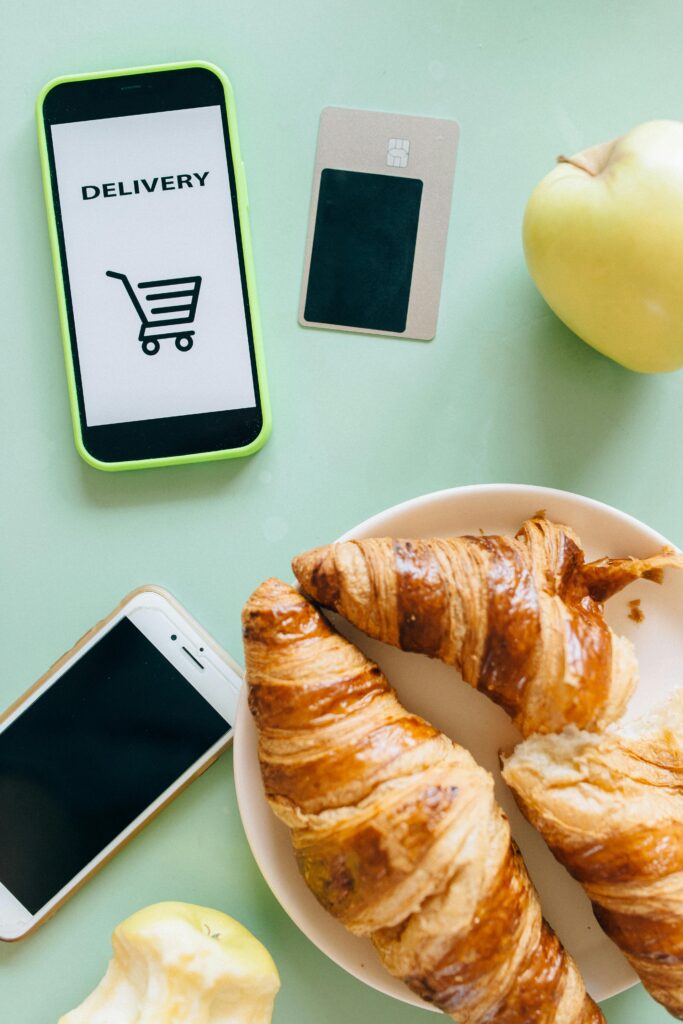 Vale-alimentação x Vale-refeição: Diferenças, Obrigações e Direitos 7 Flat lay of croissants, smartphones, and an apple showcasing a delivery concept.